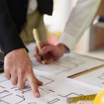 People working on paper architectural plans with computer, calculator and hardhat